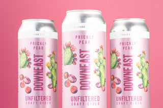 Three cans of Downeast Prickly Pear cider on a pink background